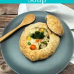 Text overlay for Pinterest. Overhead image of soup in a bread bowl on a dusty blue plate on a wooden background.