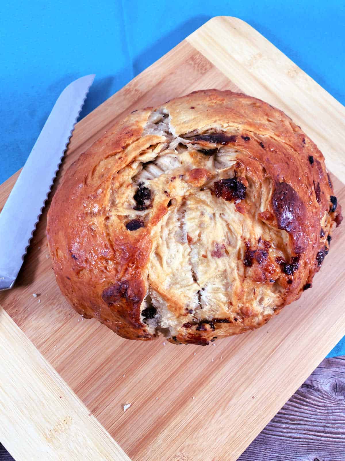 Round loaf of bread sits on a wooden cutting board with a serrated knife next to it. 