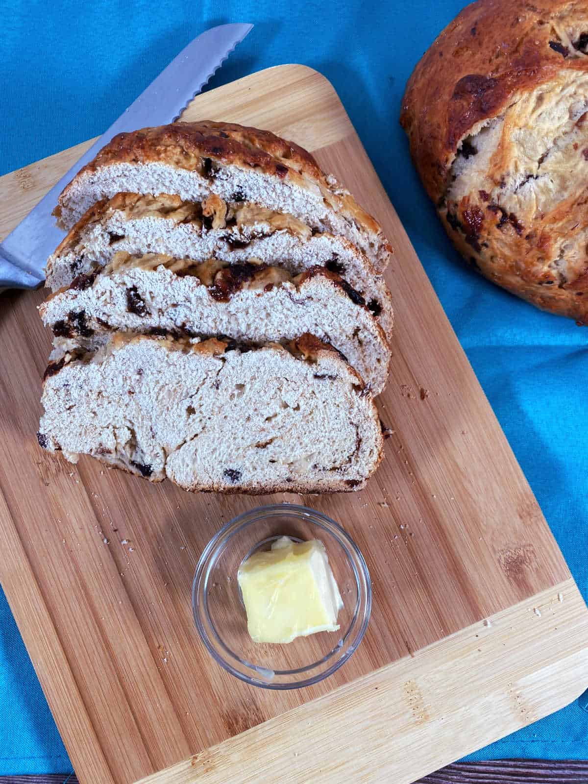 Slices of bread sit on a cutting board with softened butter in a small dish. 