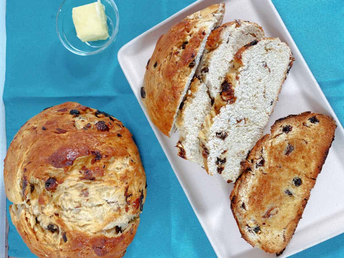 Overhead image of one loaf of bread on the left, the other, sliced and sitting on a white rectangle platter on the right. 