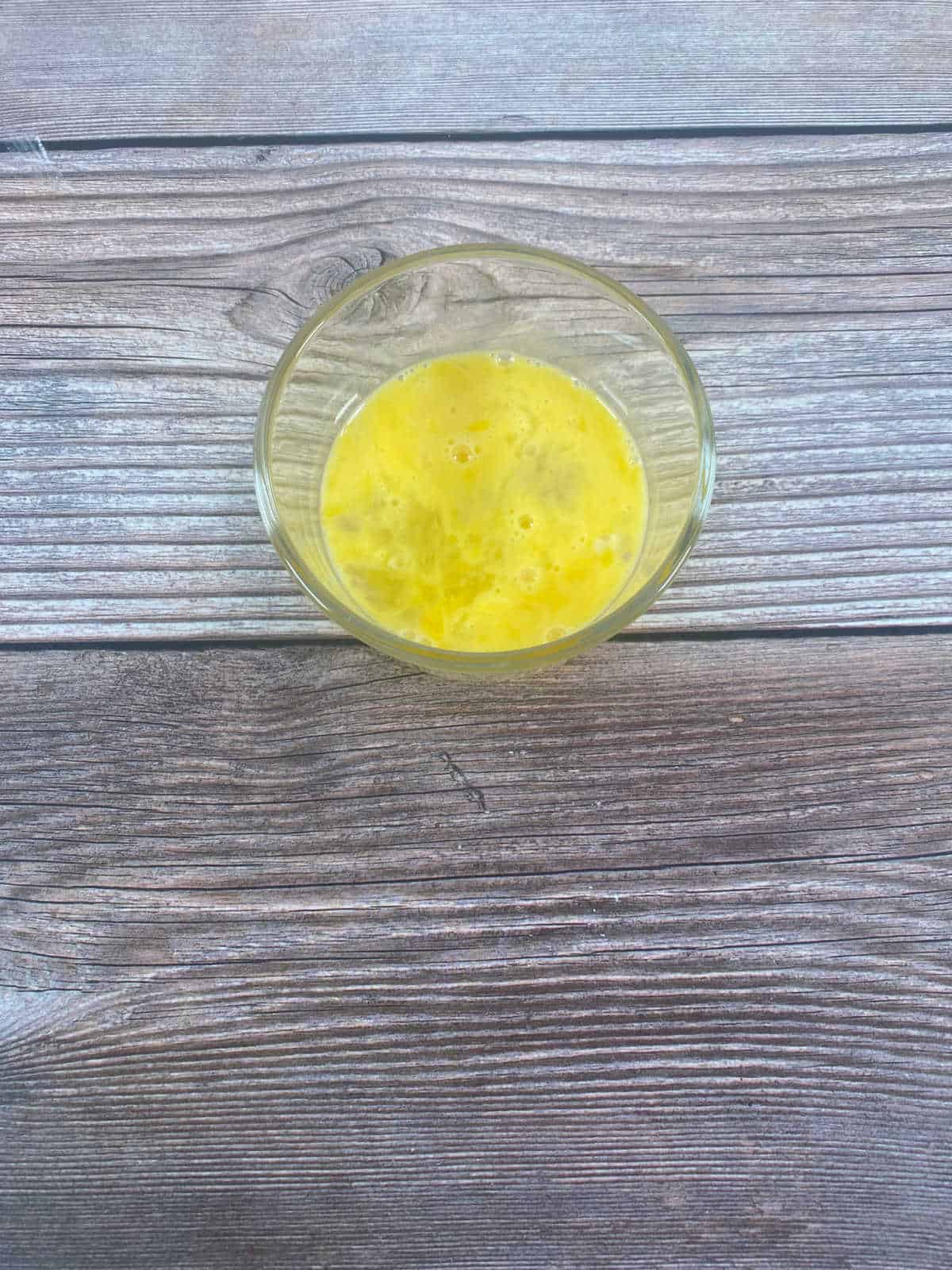 Process shot - whisked egg in a glass dish on a wooden background. 