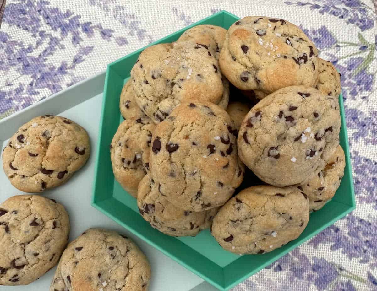 Overhead image of cookies stacked high on a mint green platter sitting on a lavender printed fabric. 