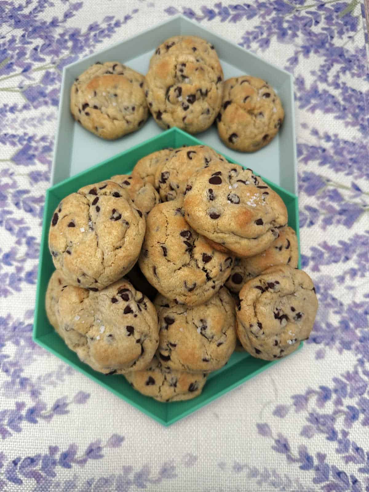 Piles of cookies stacked on a mint green platter sitting on a lavender printed cloth. 