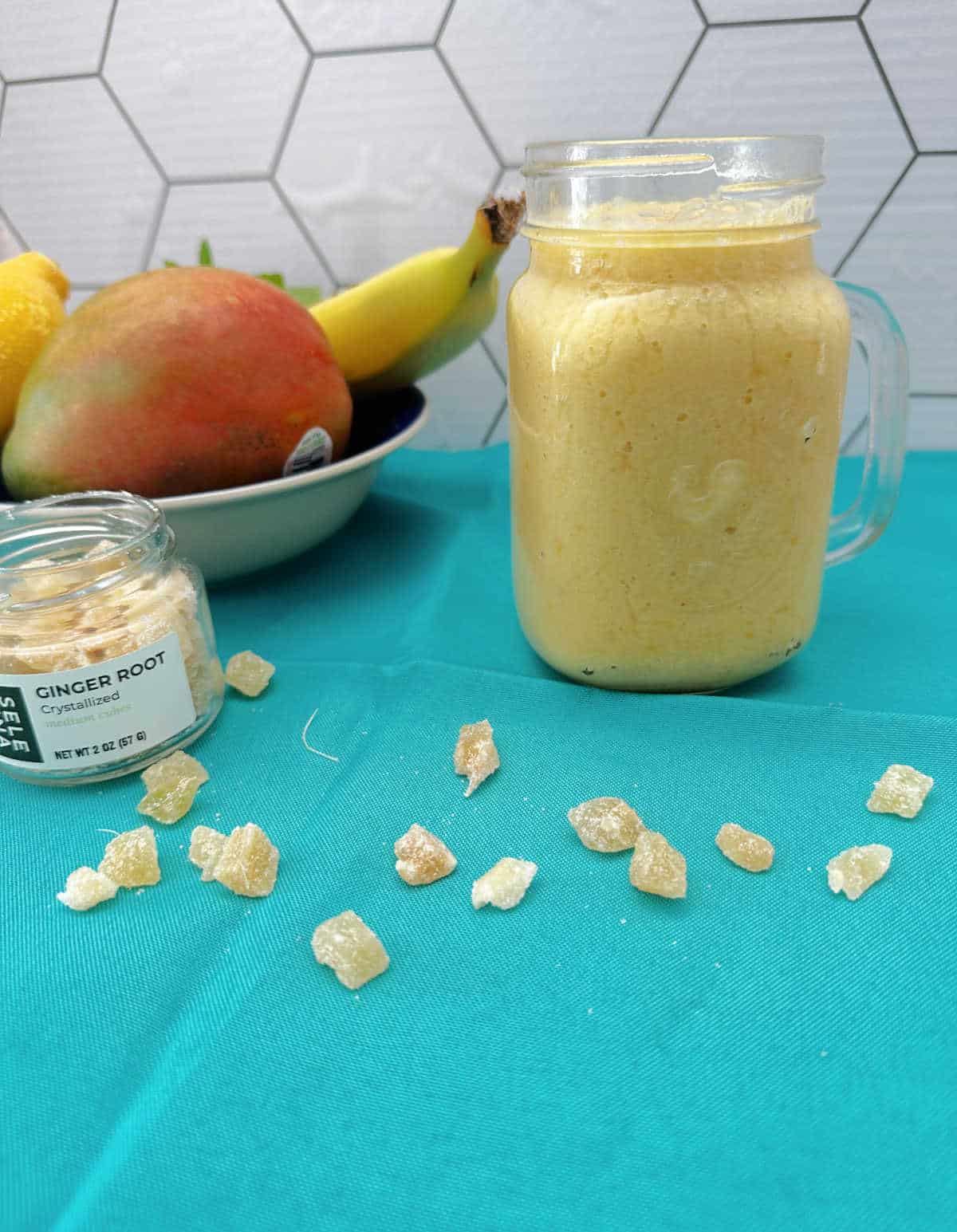 Smoothie in a mason jar with crystalized ginger pieces spread out on the teal cloth napkin in front of it. 