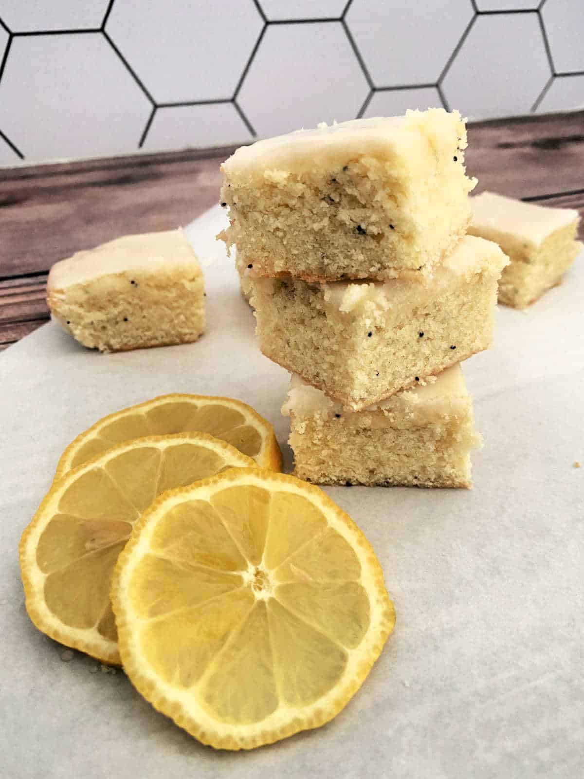 Stack of bars sit on parchment paper with lemon slices in the foreground. 