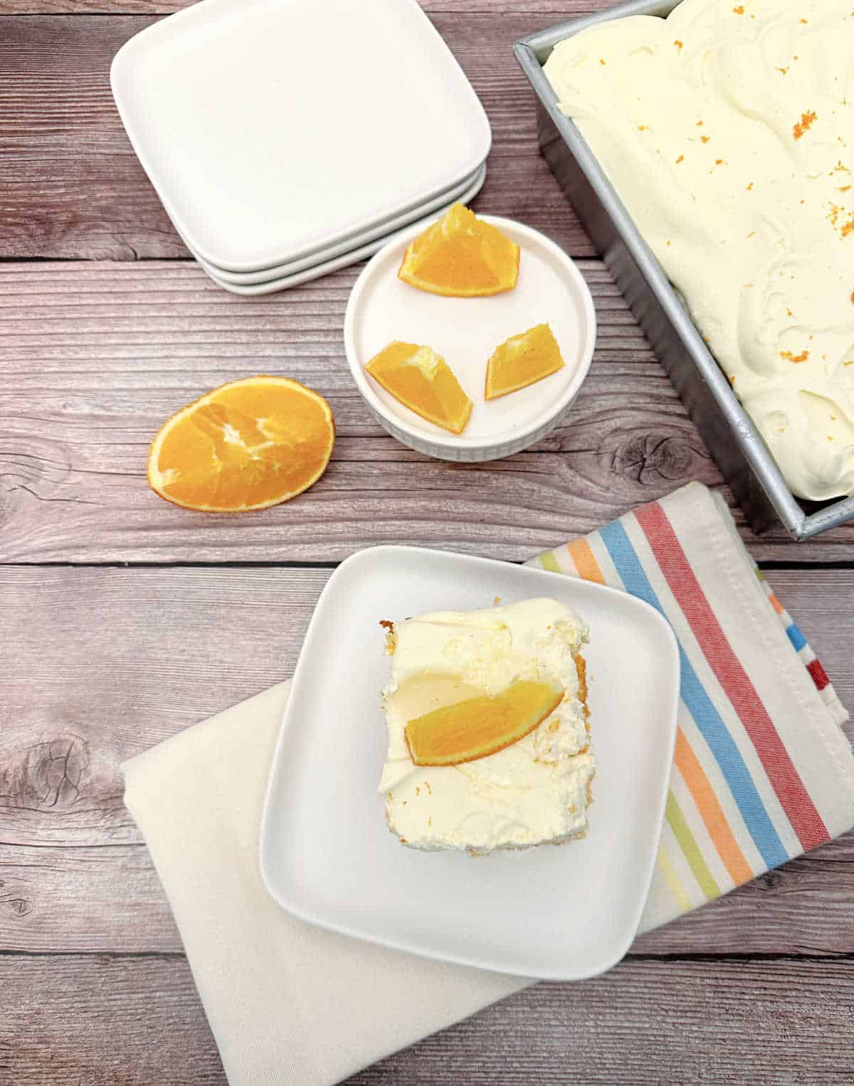 Slice of cake on a striped napkin with fresh orange segments in the background. 