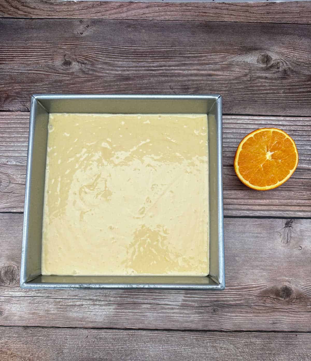 Process shot - cake batter in a pan with a halved orange next to it. 