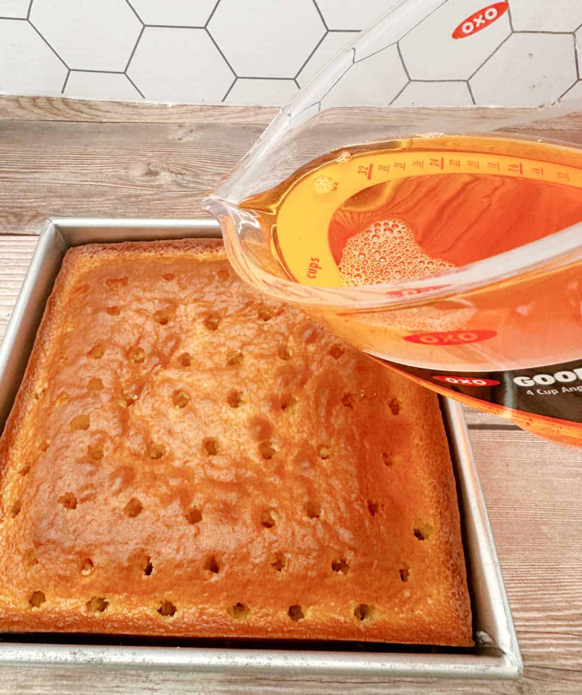 Process shot - orange jello being poured over baked cake after holes were poked into it. 