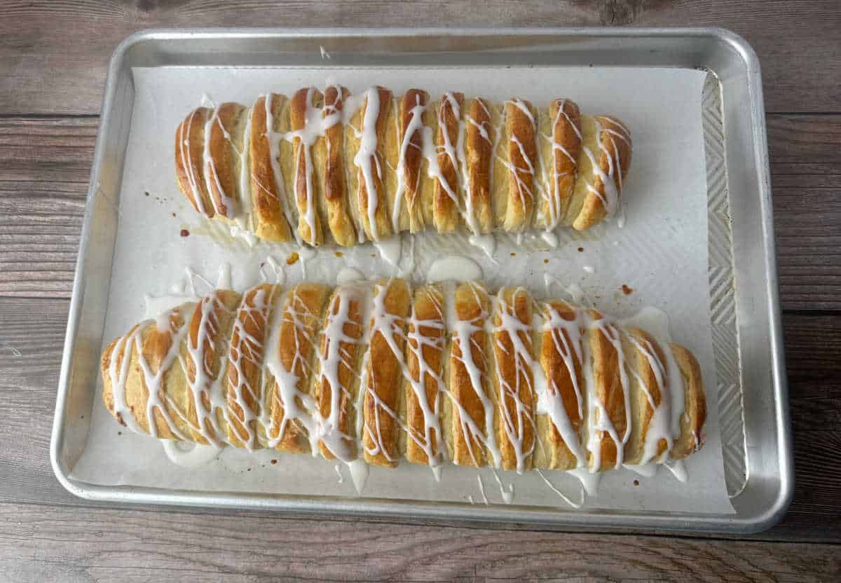 Recently glazed rolls sit side by side on a parchment lined baking sheet. 