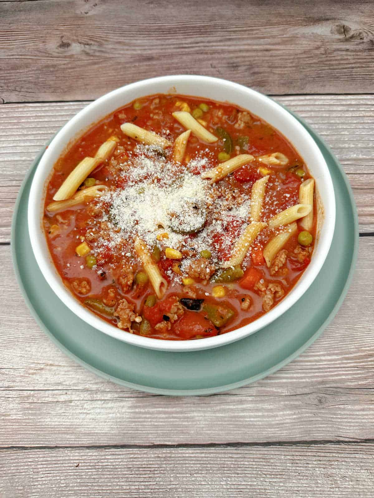 Overhead image of soup in a shallow white bowl on top of a light green plate. Soup is sprinkled with Parmesan cheese. 