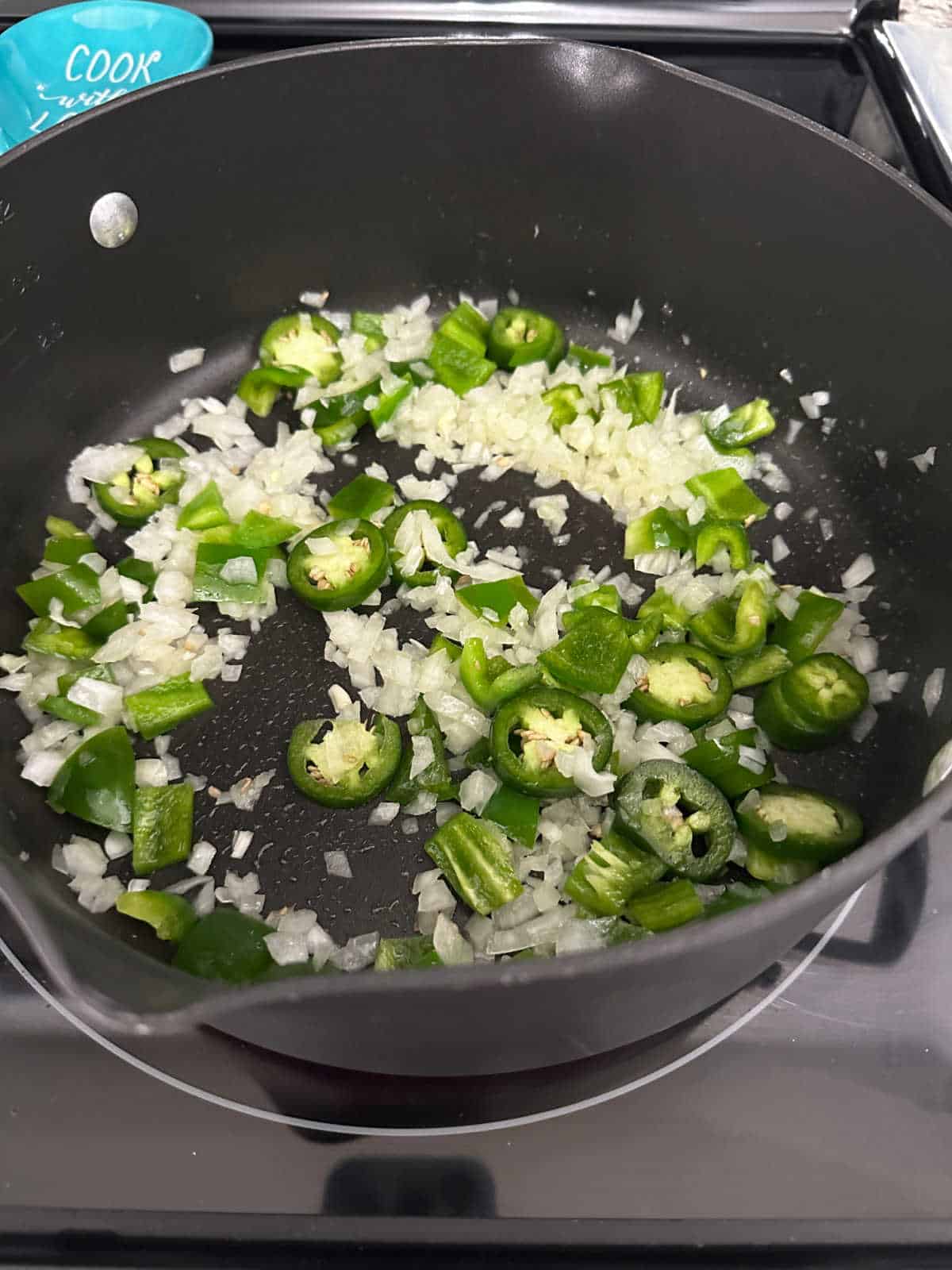 Process shot - bell pepper onion and jalapeno cooking in a large saucepan. 