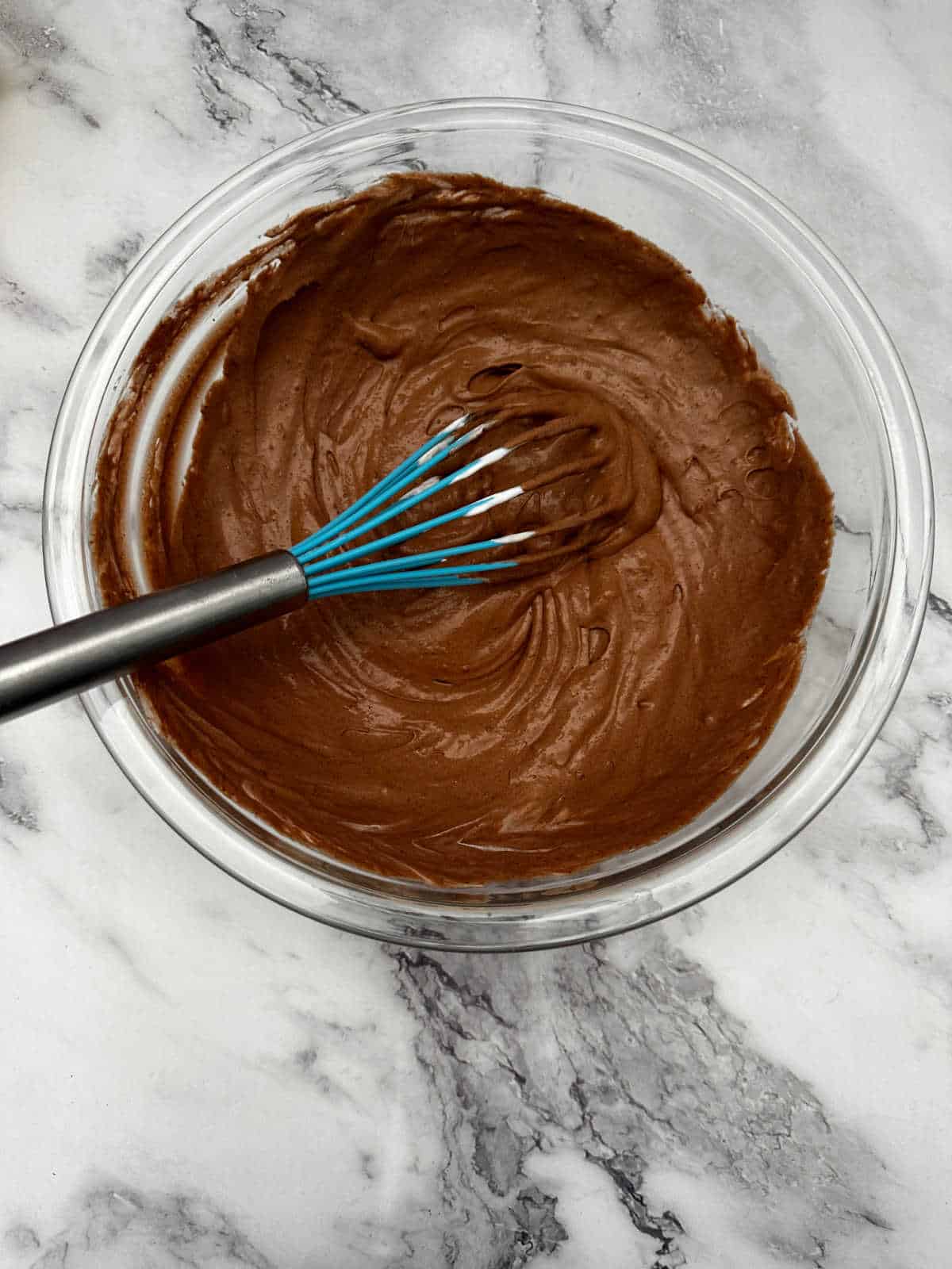 Process shot - pudding, milk and whipped topping mixed together in a glass bowl with a blue silicone whisk.