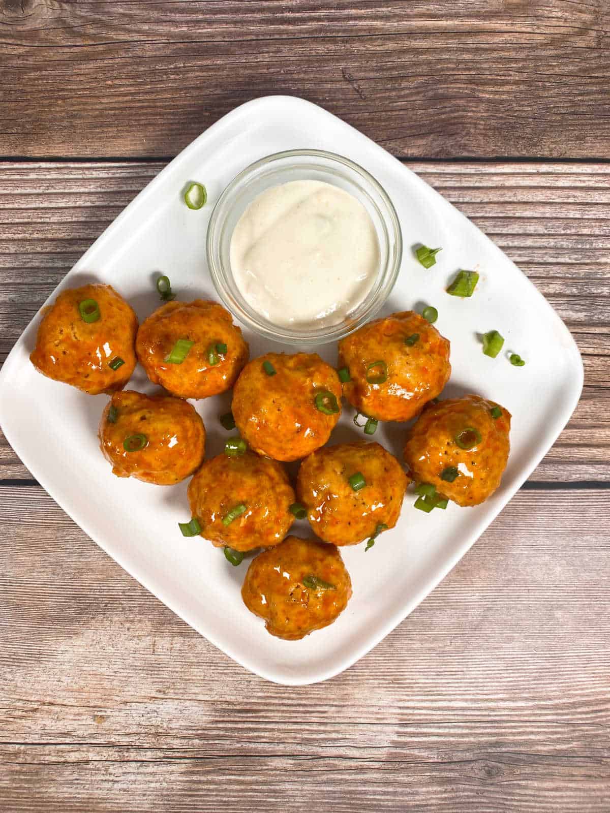 Overhead image of meatballs on a white plate, garnished with green onions and sitting with a bowl of blue cheese dressing. 