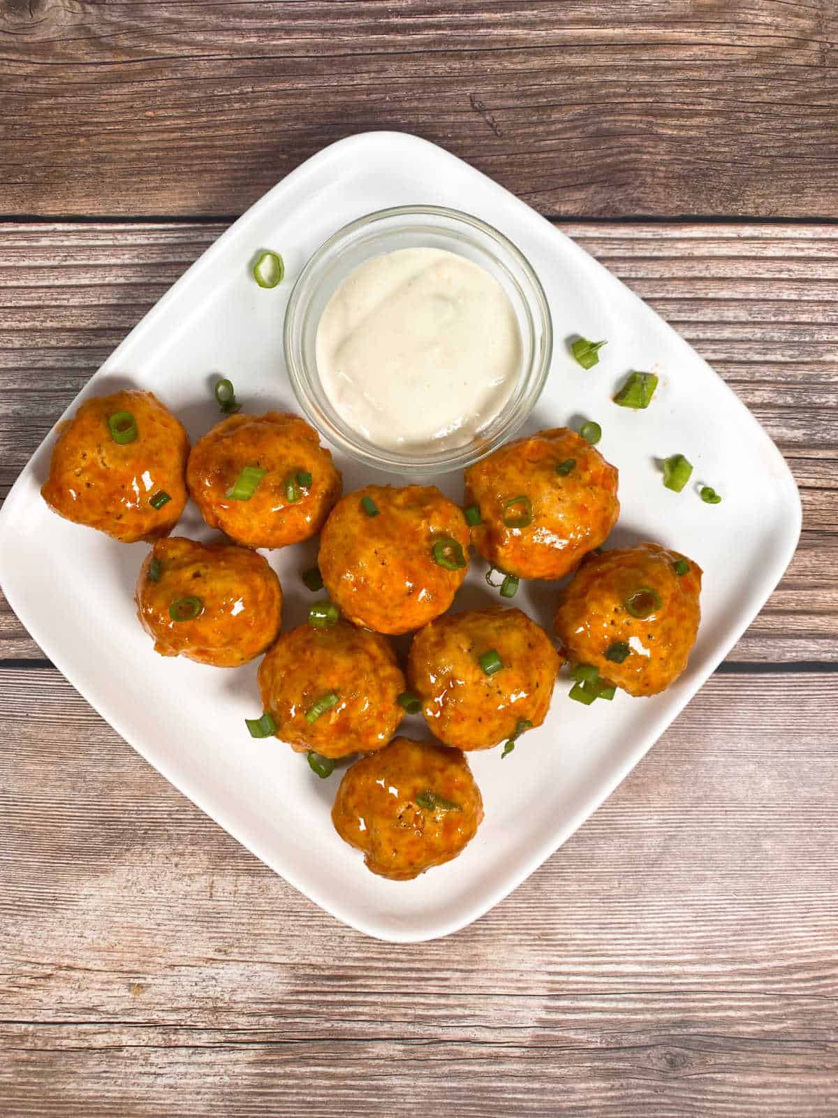 Overhead image of meatballs on a white plate, garnished with green onions and sitting with a bowl of blue cheese dressing.