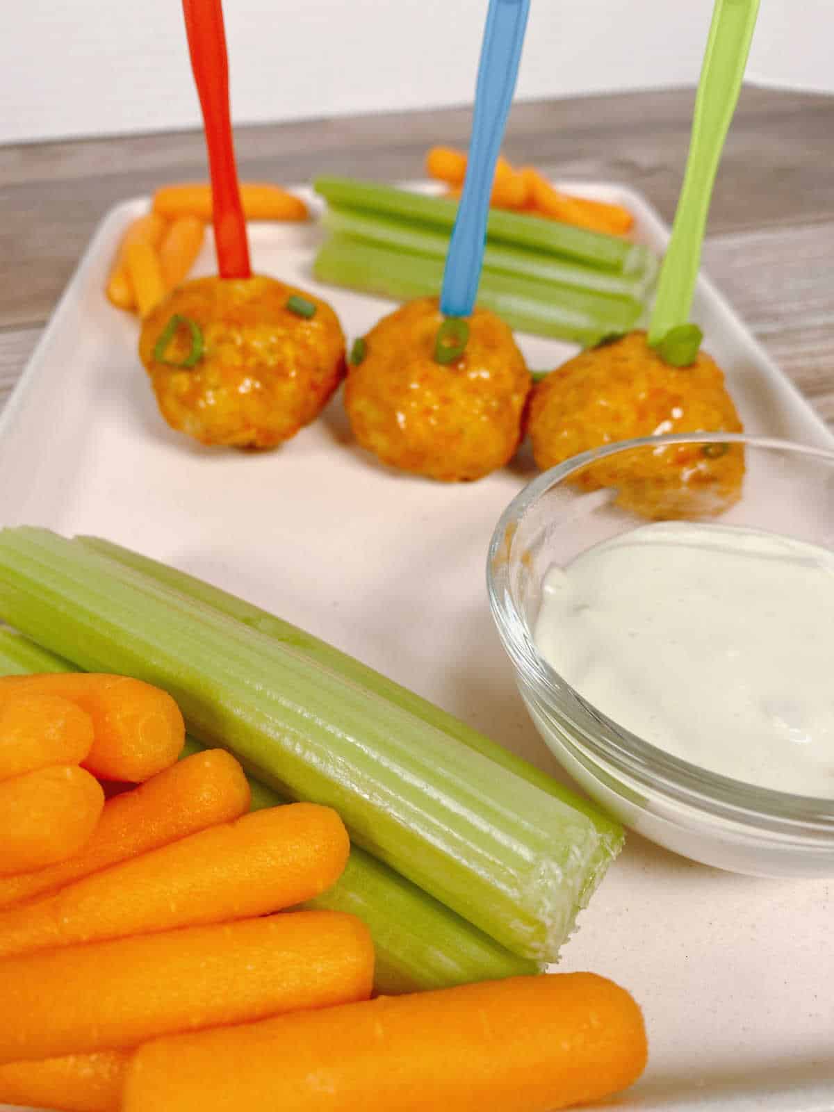 Meatballs on a pink platter with celery sticks, carrots and blue cheese dressing. 