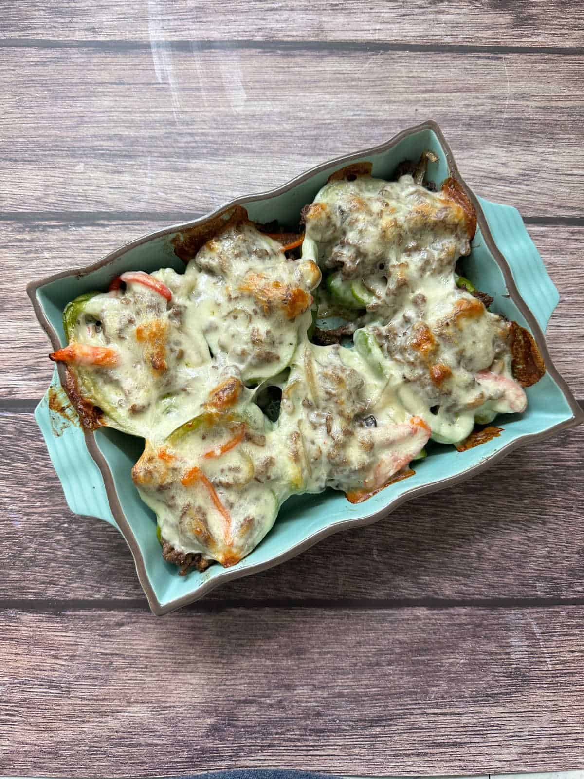 Overhead image of baked stuffed peppers with cheese melted on top and vegetables peeking through. 