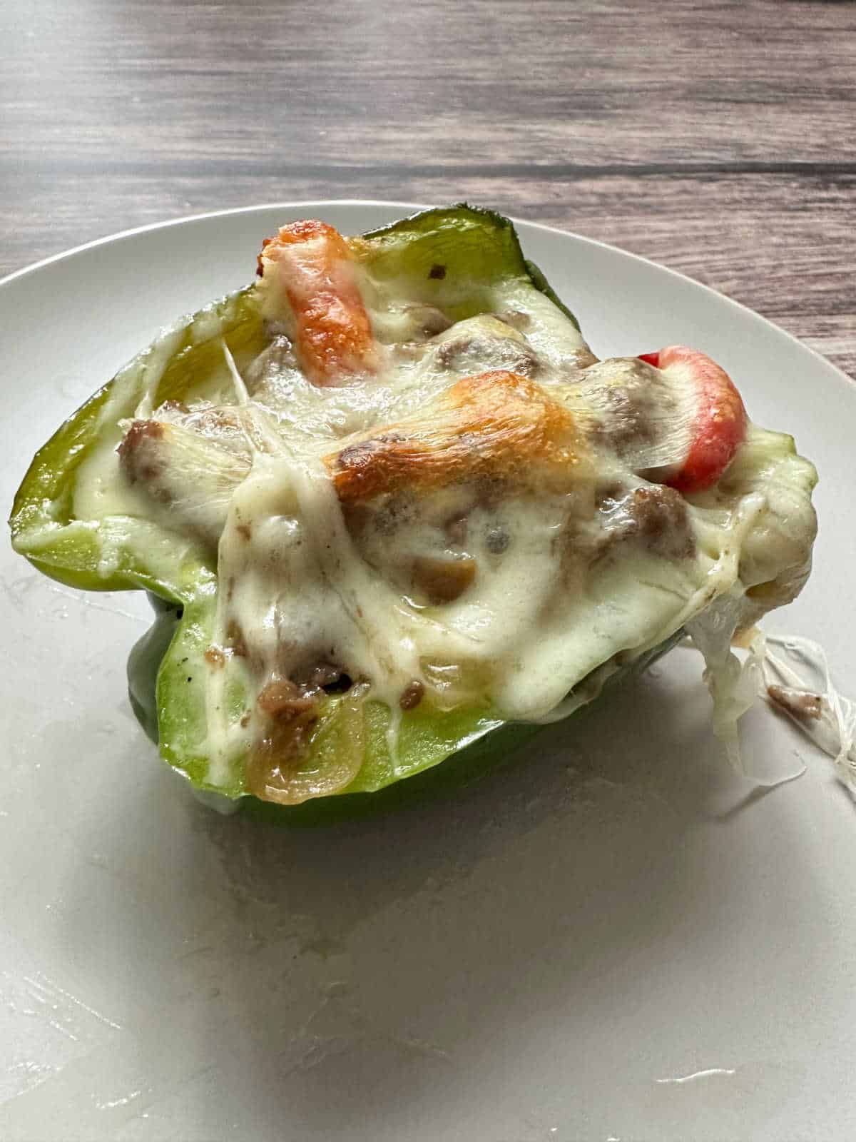 Close up image of cheese topped stuffed pepper on a white plate. 