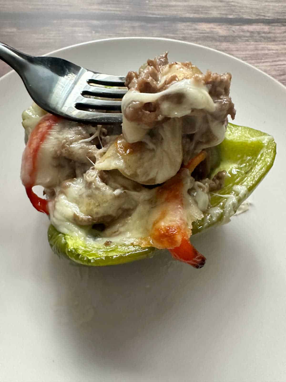 Fork lifting steak and cheese out of baked stuffed pepper. 