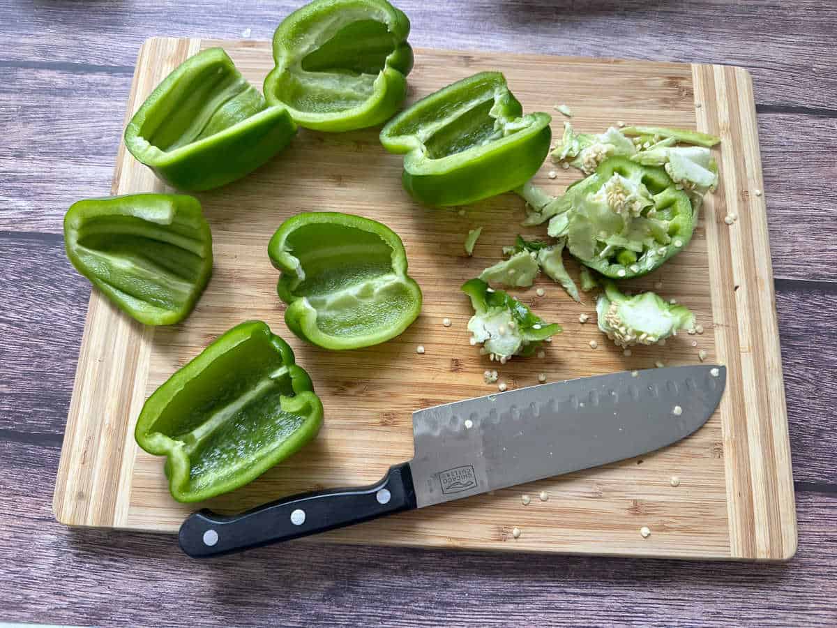 Process shot - Halved bell peppers sit on a wooden cutting board. 