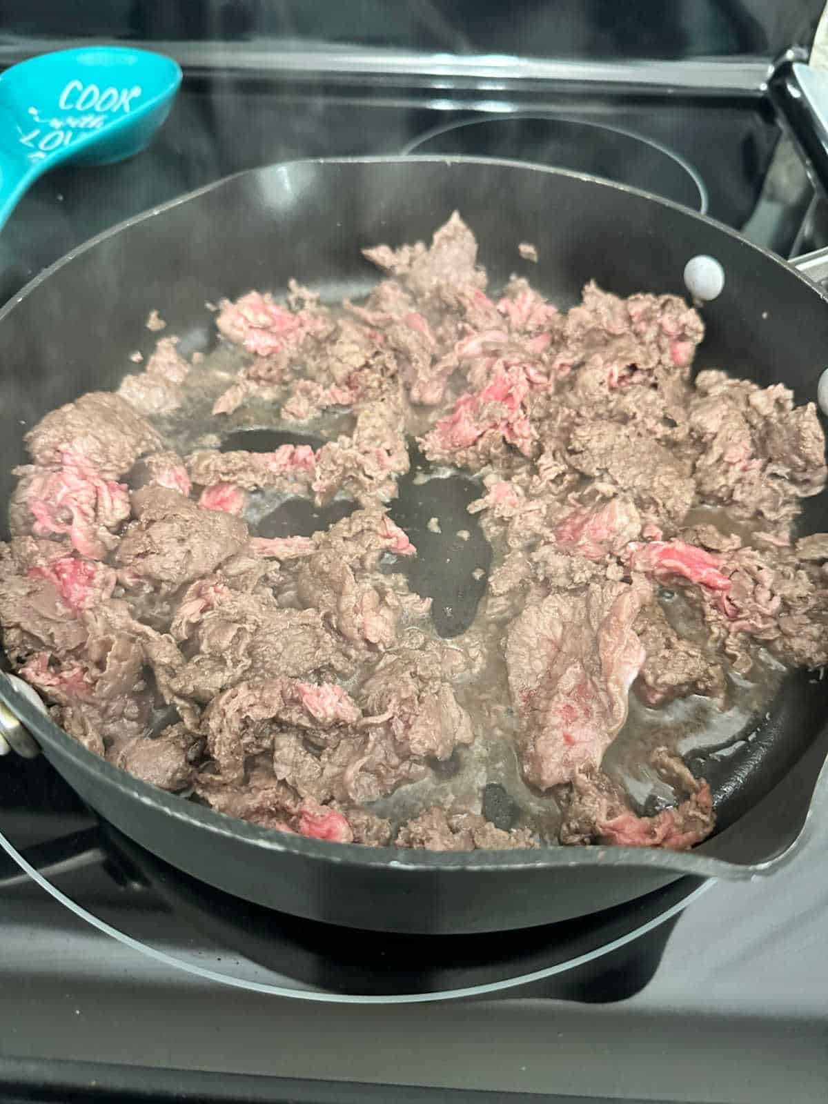 Process shot - shaved steak cooking in skillet on stove. 