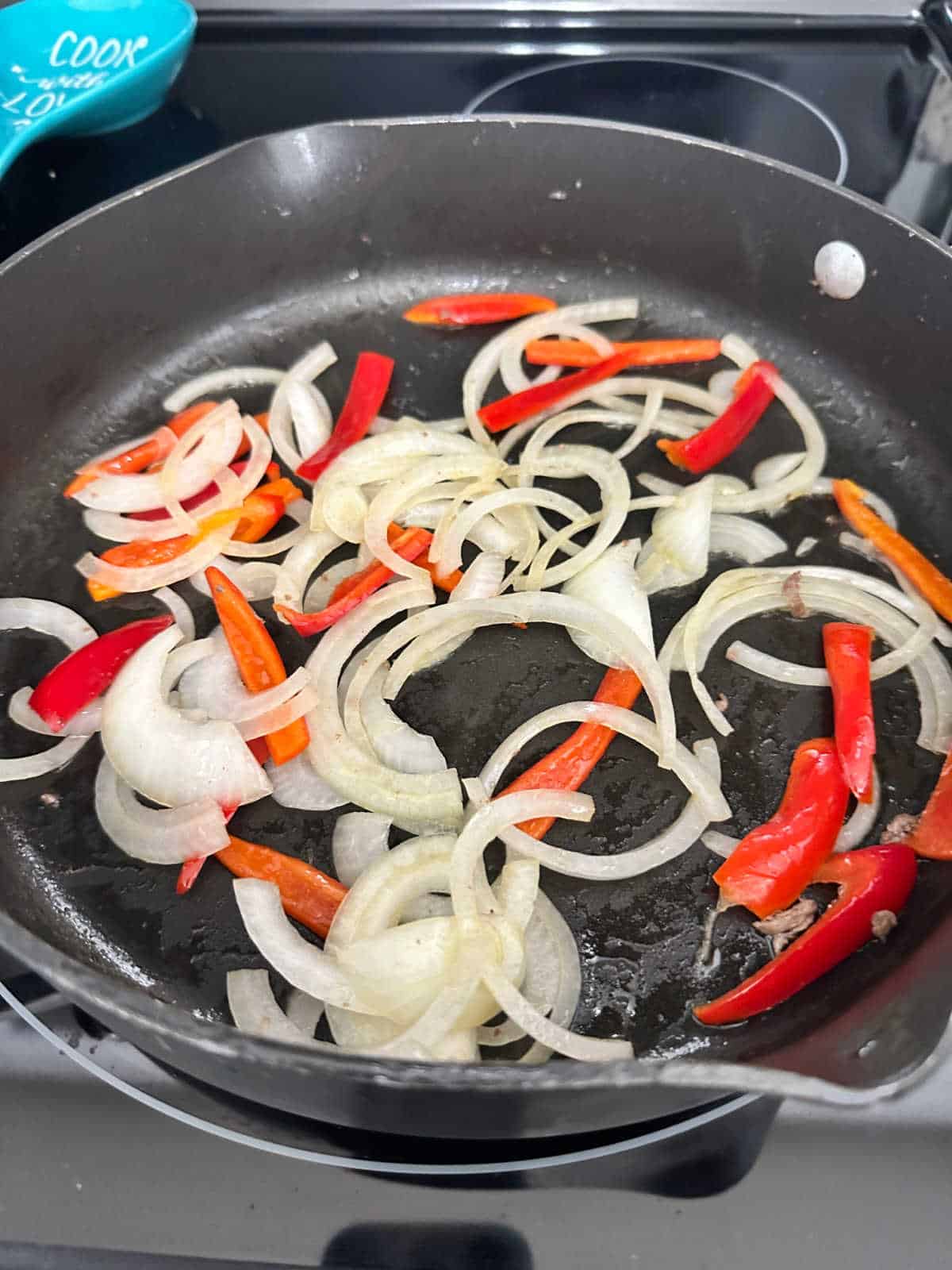 Process shot - bell pepper and onions cooking in skillet on stove. 