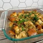 Baked stuffing topped with parsley in a glass dish on a wooden background.