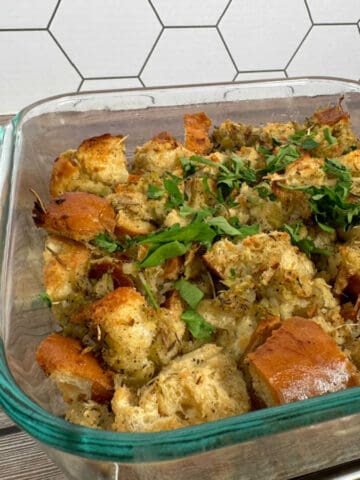 Baked stuffing topped with parsley in a glass dish on a wooden background.