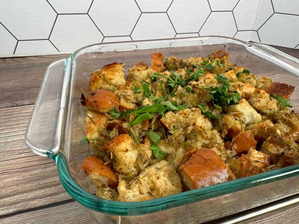 Baked stuffing topped with parsley in a glass dish on a wooden background.