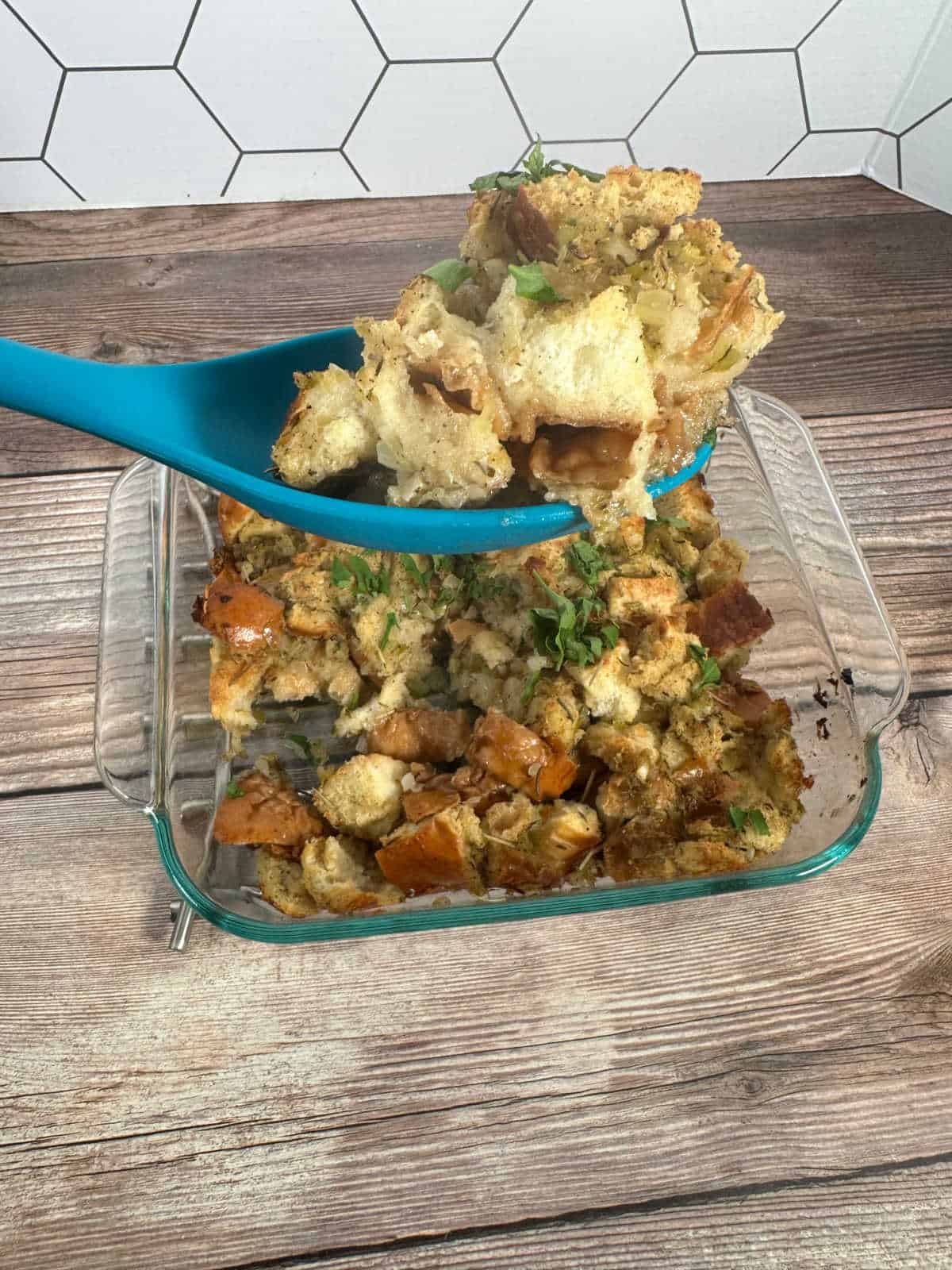 Spoonful of stuffing held above the casserole dish on a wooden background.