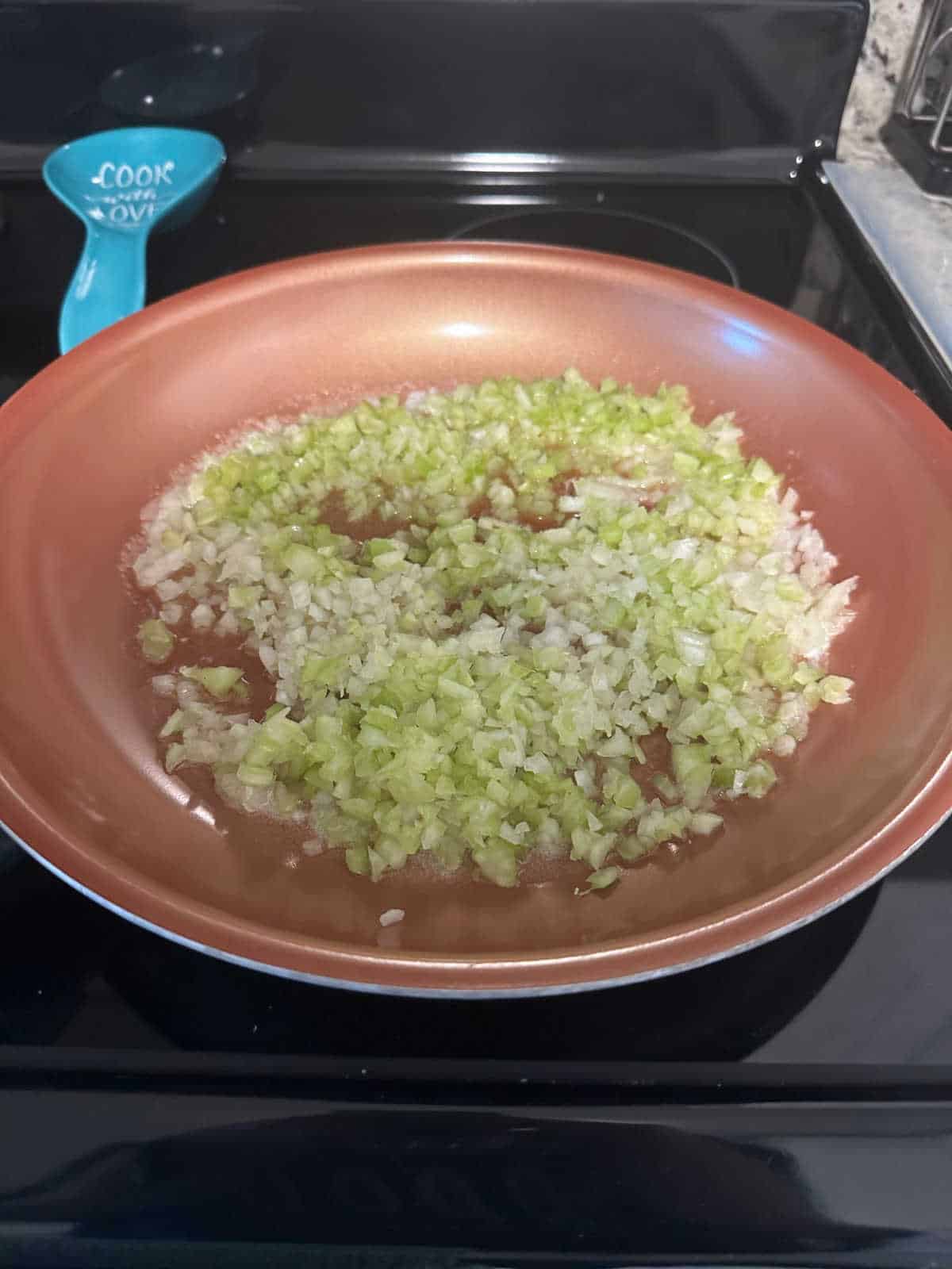 Process photo: Celery and onion cooking in a copper colored skillet on the stove.