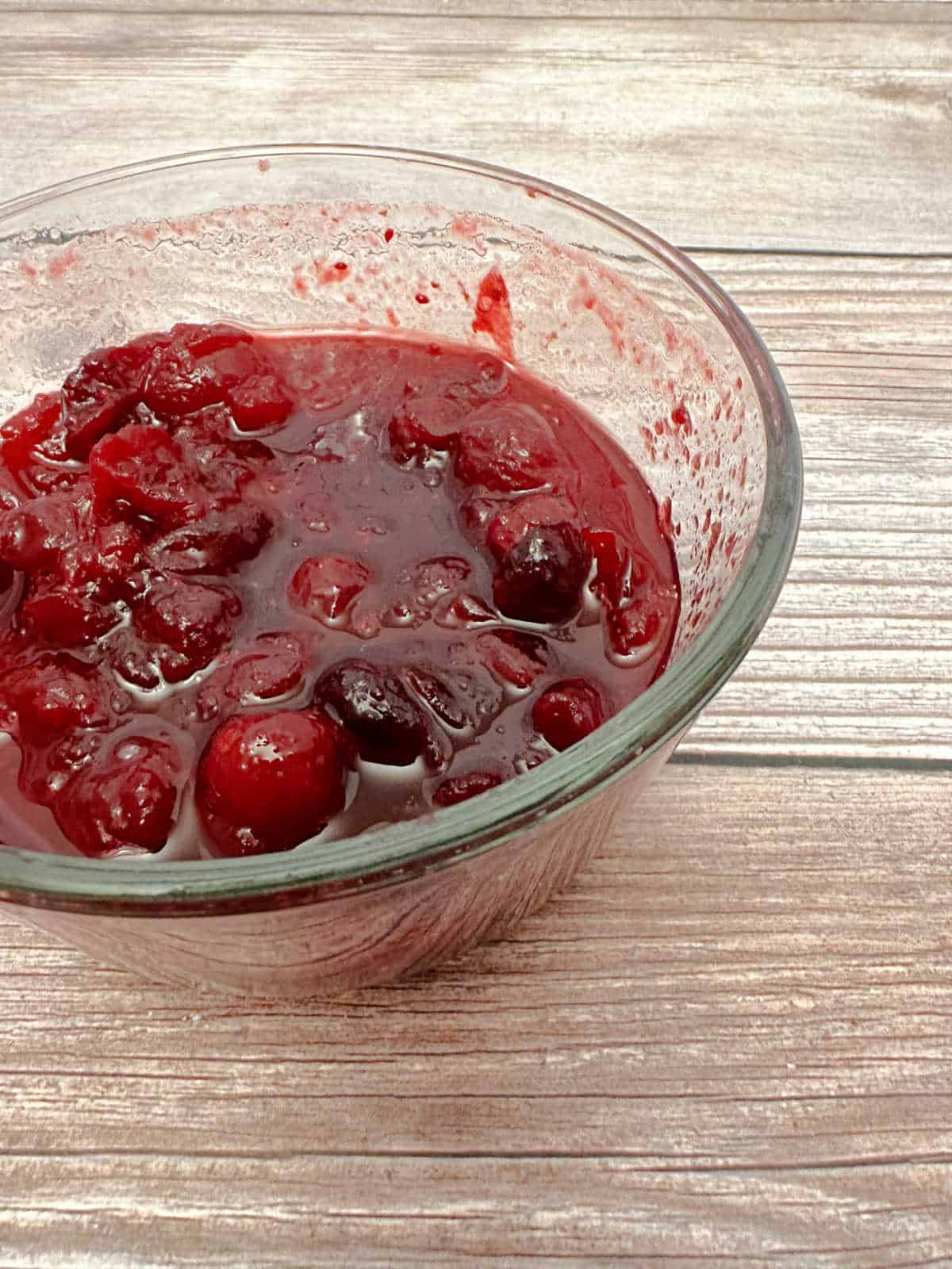 Cranberry sauce in a glass dish on a wooden background.