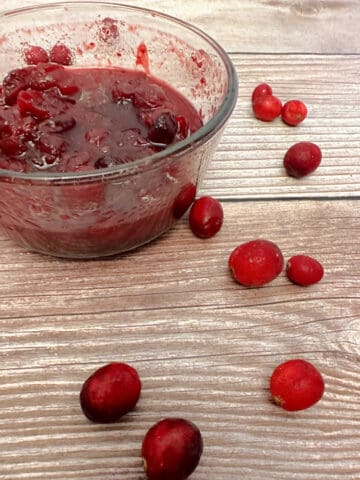 Cranberry sauce in a glass dish surrounded by fresh cranberries.