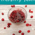 Image for Pinterest with text overlay. Glass bowl of cranberry sauce surrounded by fresh cranberries sits on a wooden background.