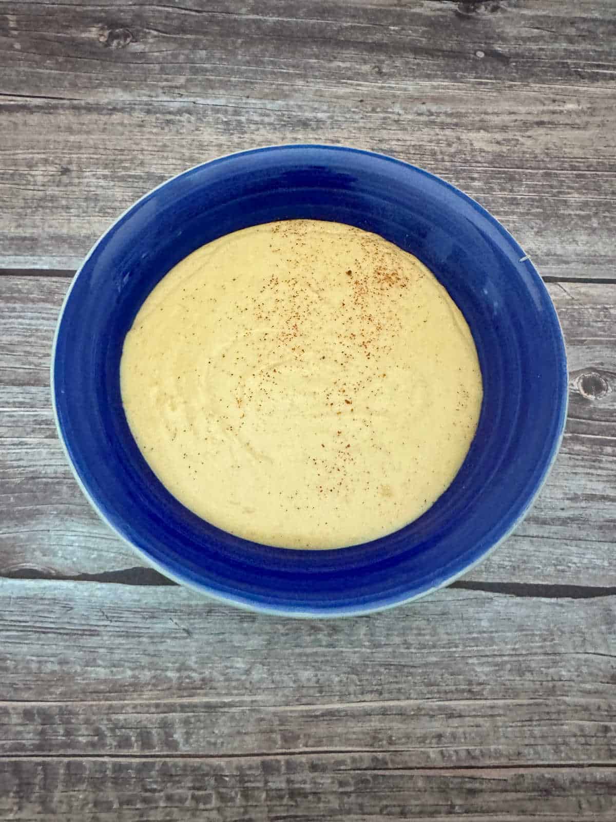 cheese sauce sits in a blue bowl on a wooden background. 