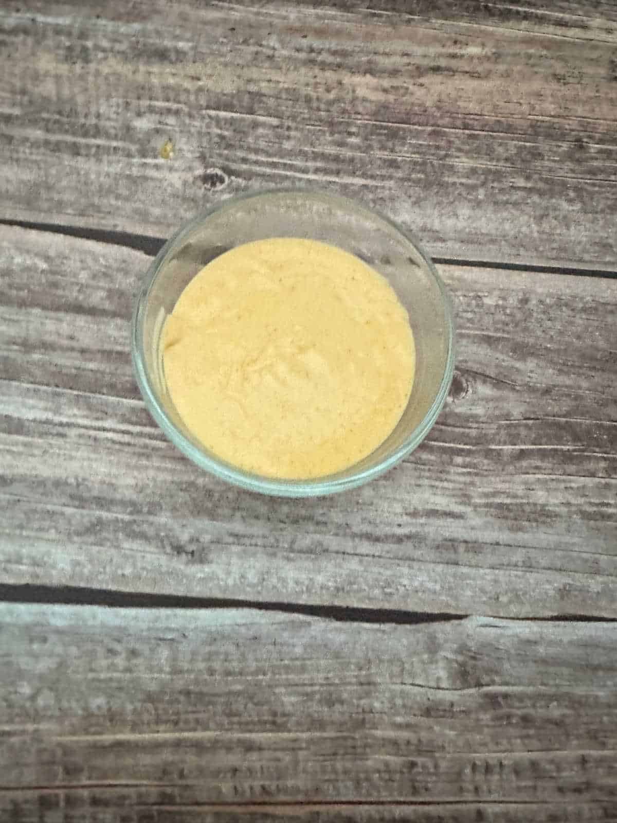 Cheese sauce in a glass bowl on a wooden background. 