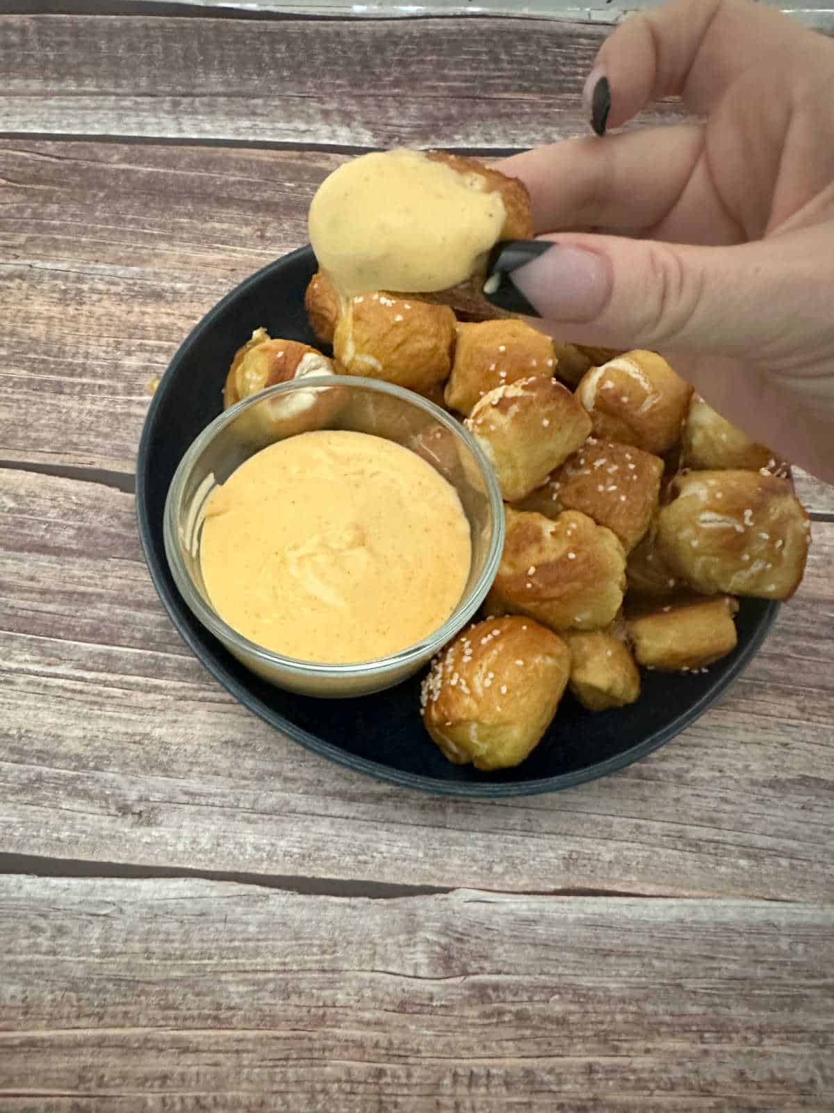 Close up of soft pretzel being dipped into cheese sauce. 