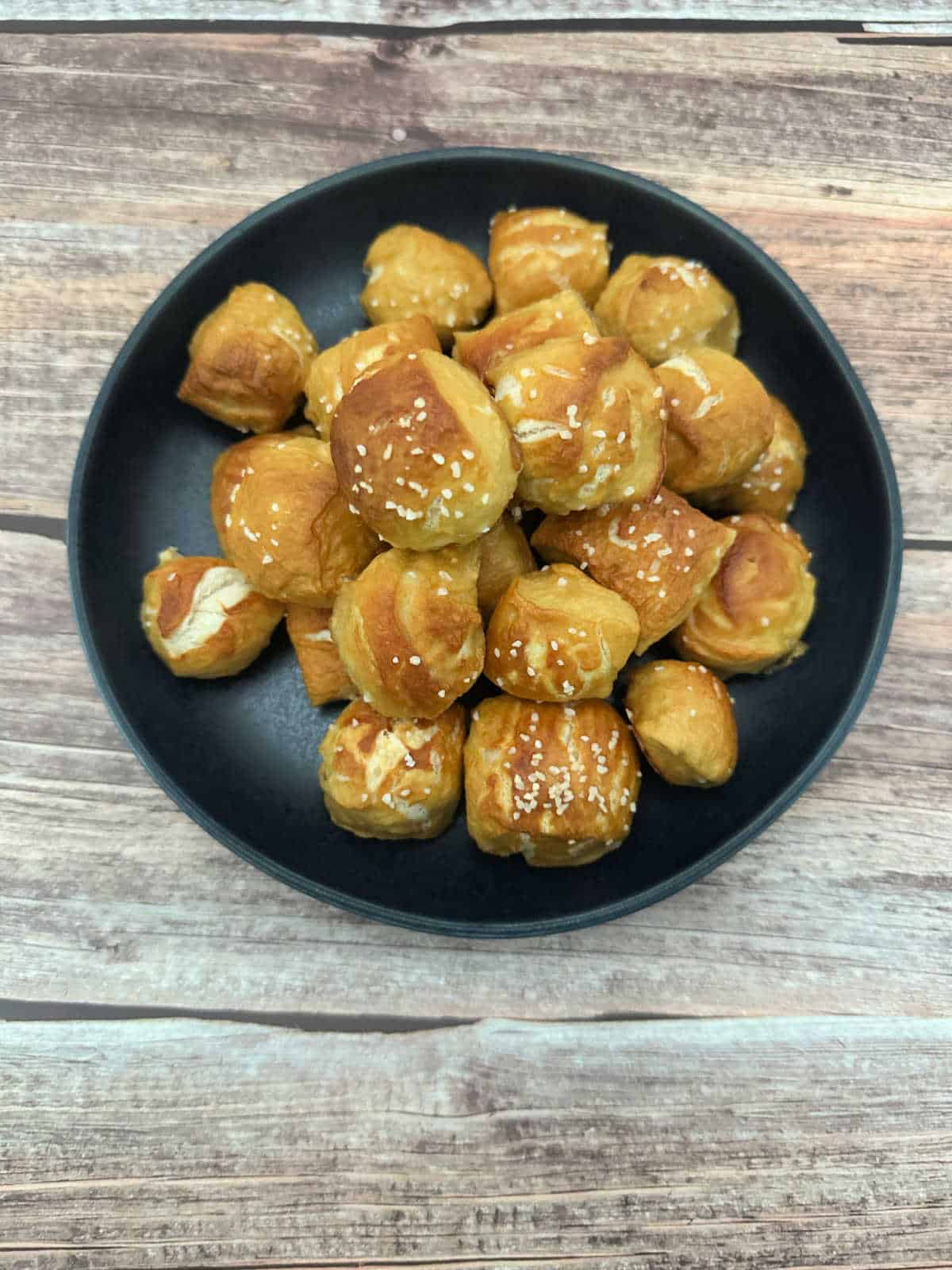 Overhead image of pretzel bites stacked high on a round plate on a wooden background. 