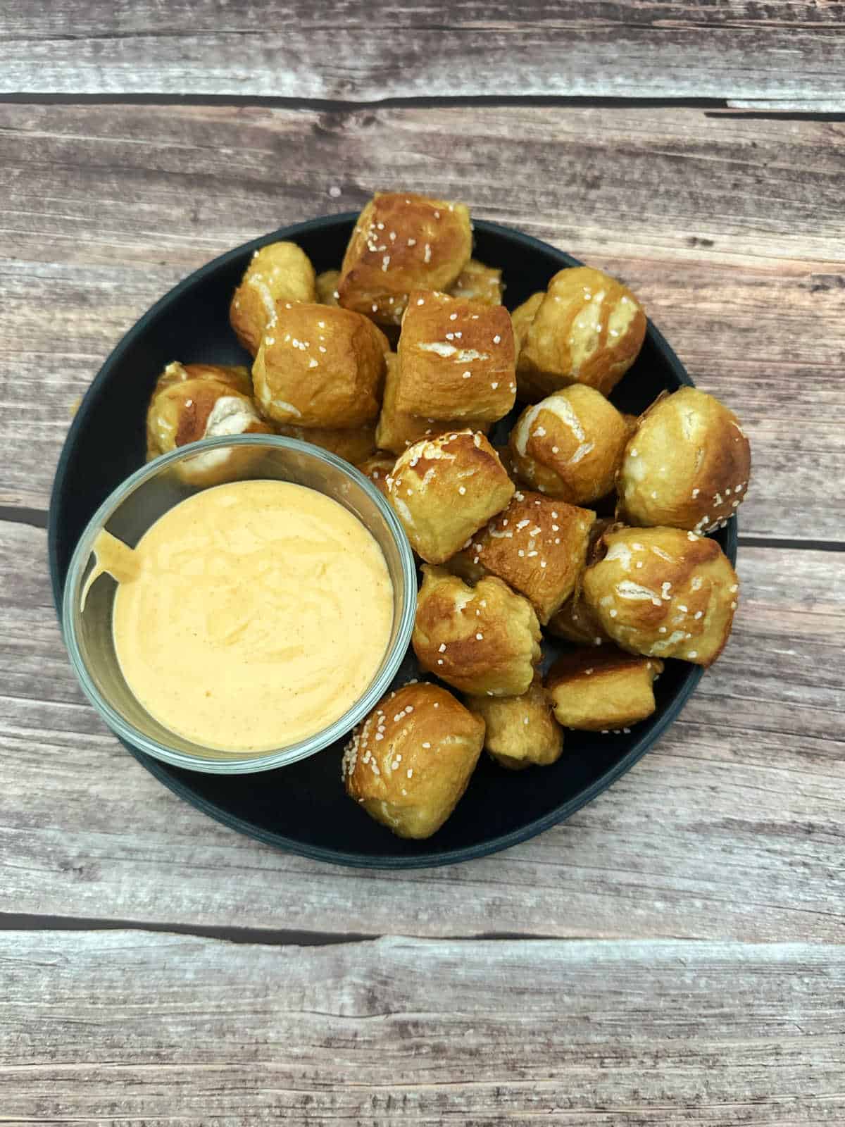 Overhead image of soft pretzel bites piled high on a round plate with a bowl of spicy cheese sauce on the side.