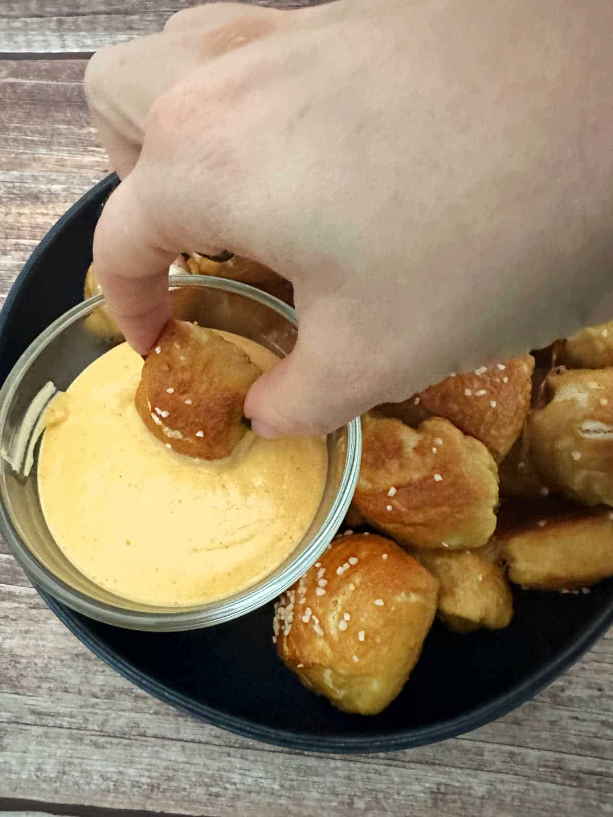 Pretzel bite being dunked into spicy cheese sauce. 