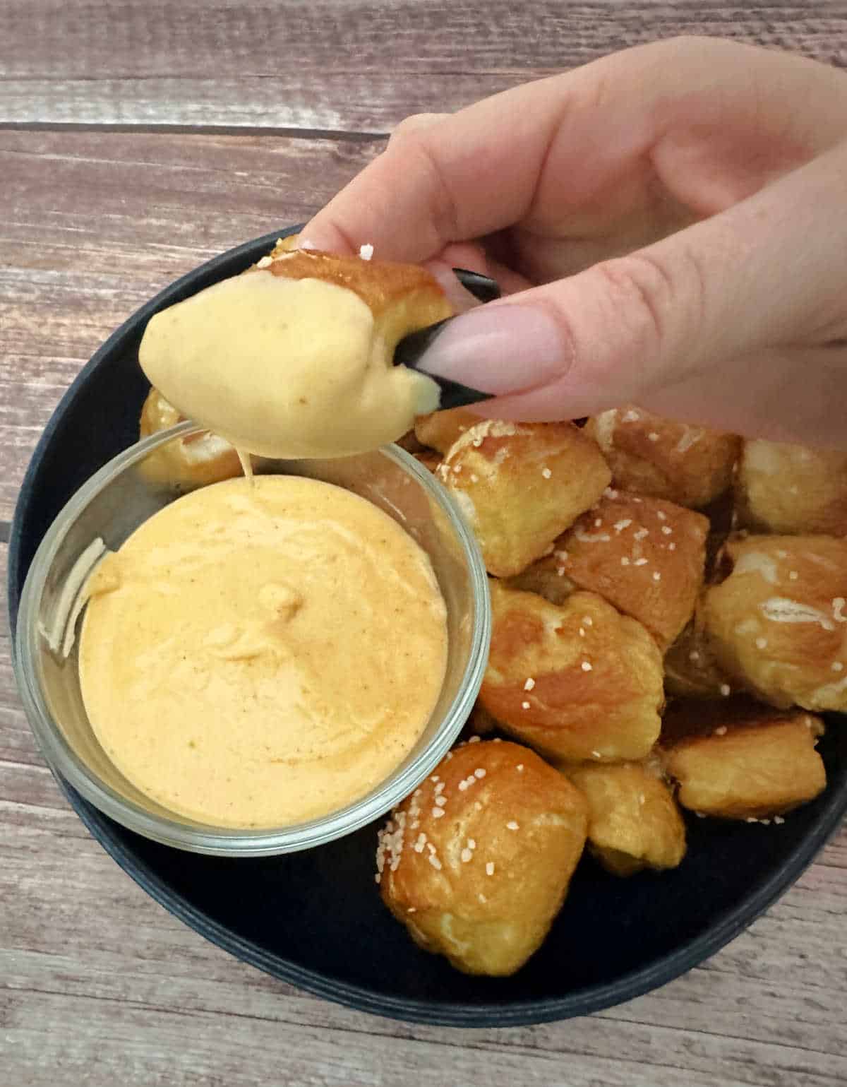 Overhead image showing pretzel bite being dipped into spicy cheese sauce. 