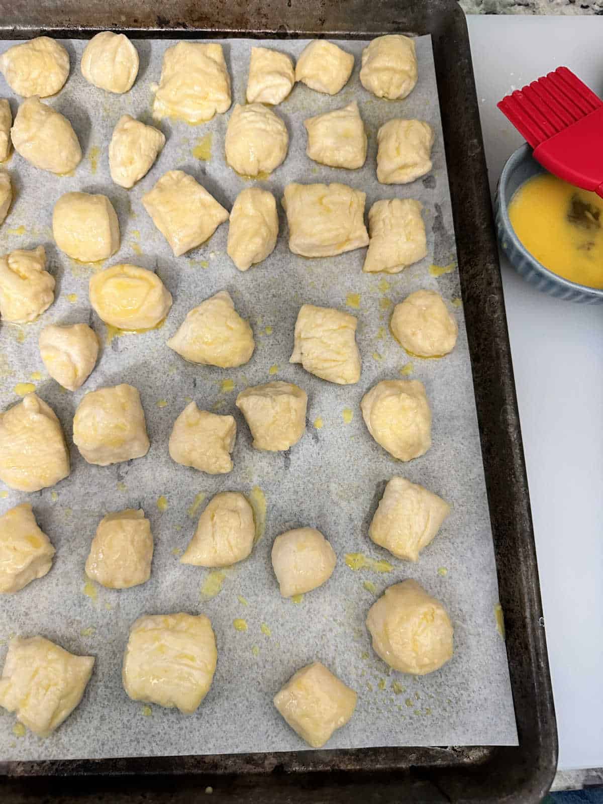 Process photo - Pretzel bites brushed with egg wash on a baking sheet. 