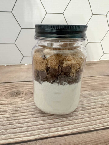 Mason jar of cookie mix - flour and granulated sugar layered on the bottom, topped with chocolate chips and then brown sugar on top. 