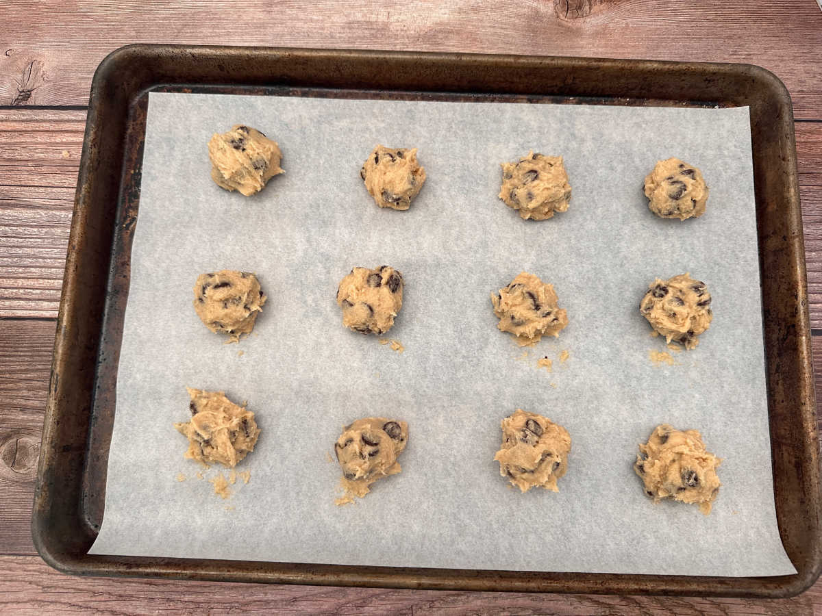 Dollops of cookie dough on a parchment lined baking sheet ready to be baked. 